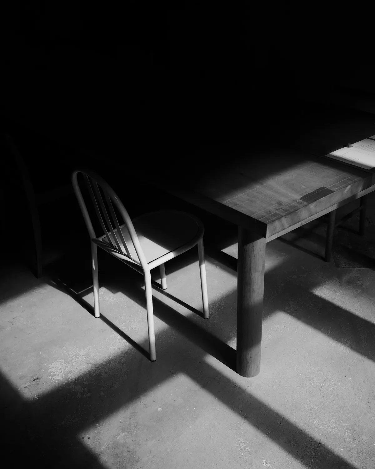 A single chair at a table in a dark room lit by a shaft of window light