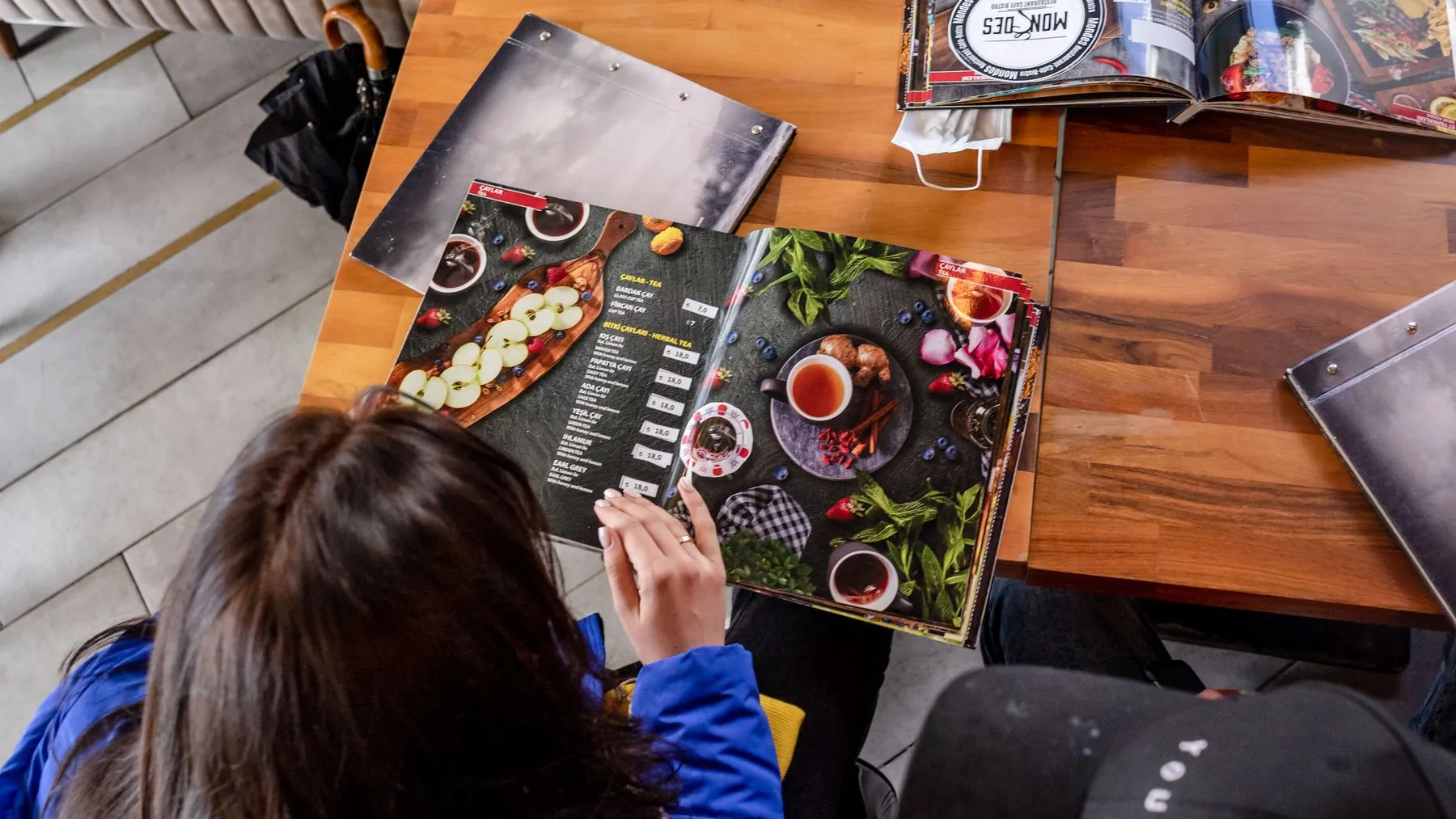 Guests reading a menu at a sunlit wooden table in a restaurant